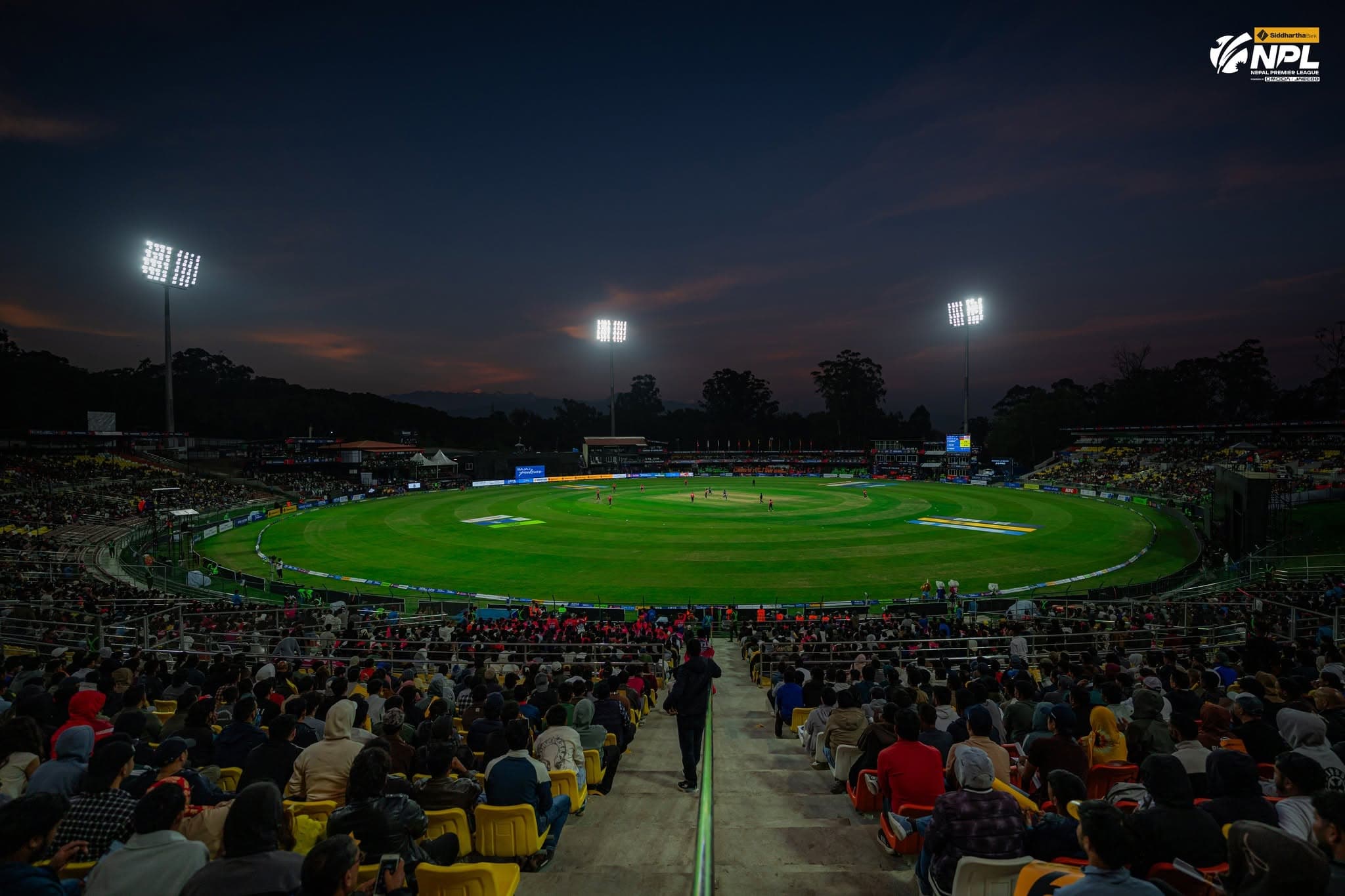 A view of the Tribhuvan University International Cricket Ground in Kirtipur filled with spectators at dusk.