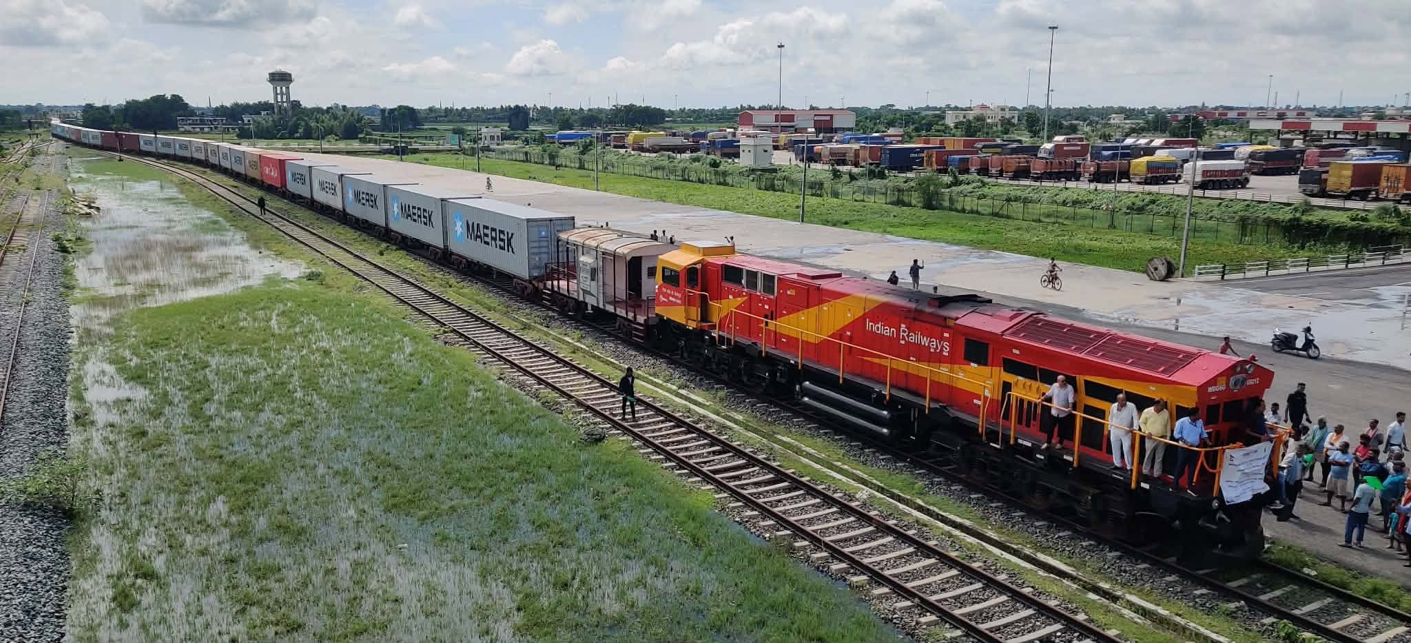 A freight train carrying shipping containers moves along tracks at a logistics facility.