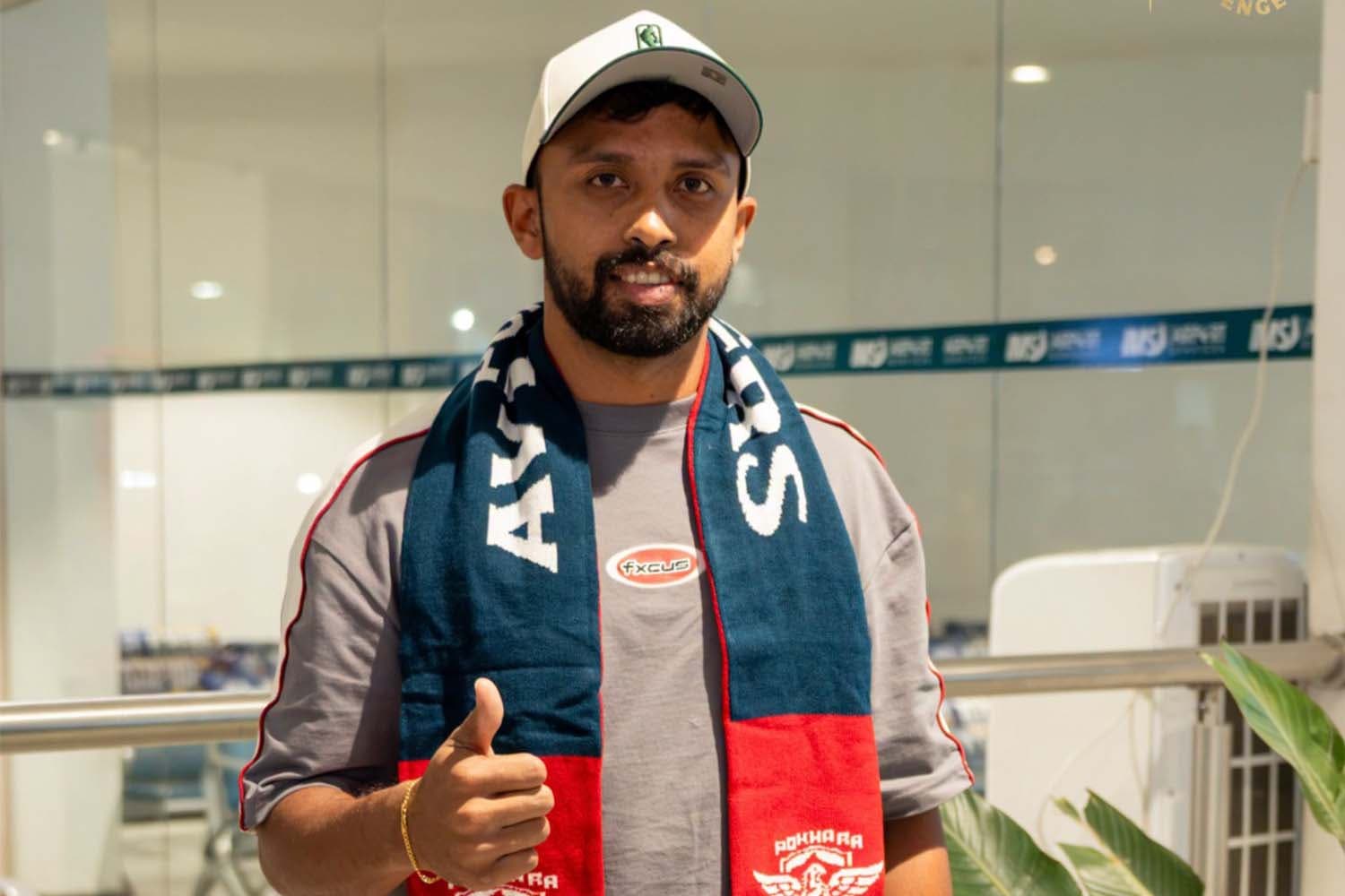 A cricketer wearing a Pokhara Avengers scarf and cap giving a thumbs up.