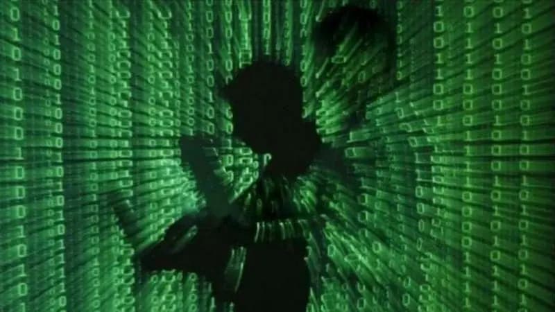 A silhouette of a person using a laptop against a background of digital code.