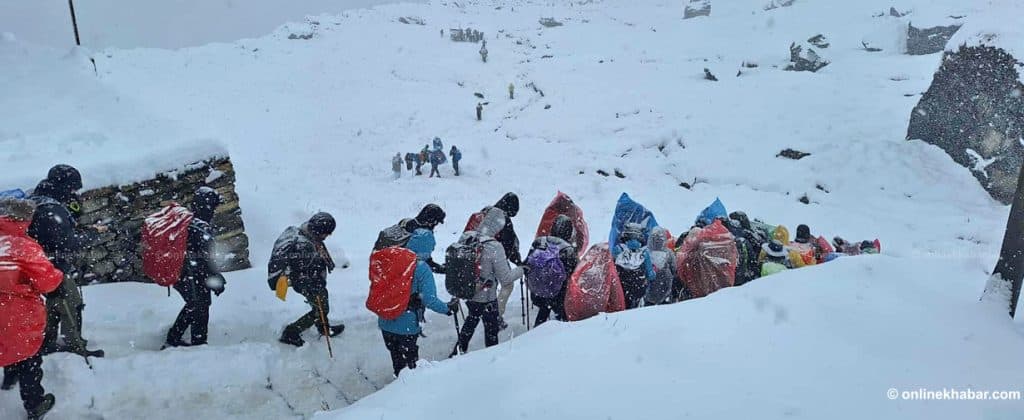 A group of trekkers with large backpacks walking through a snow-covered mountain path.