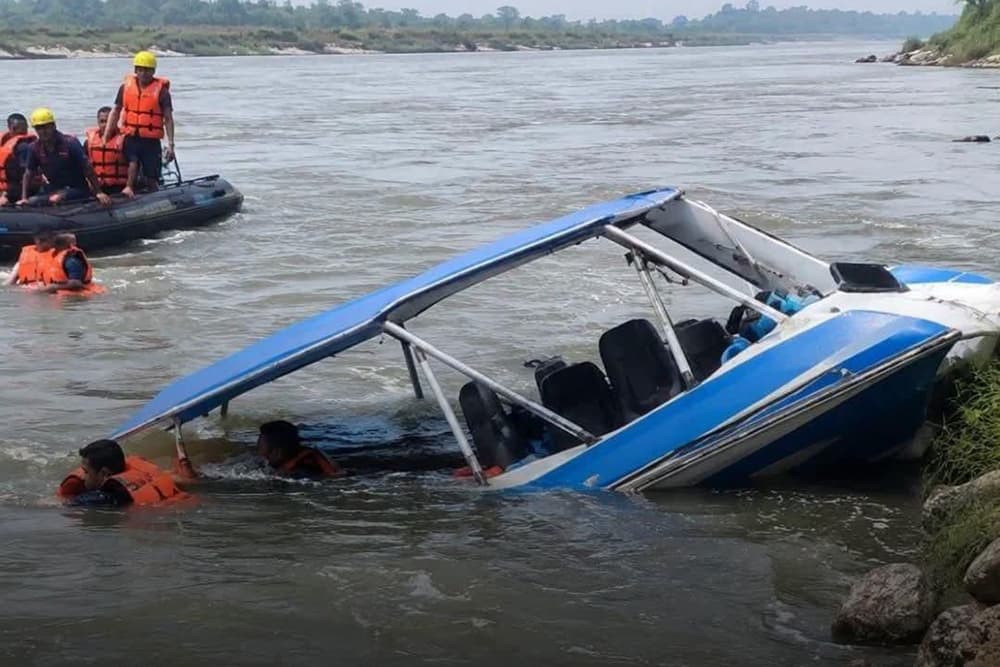 A capsized motorboat in the Saptakoshi River with rescue workers nearby.