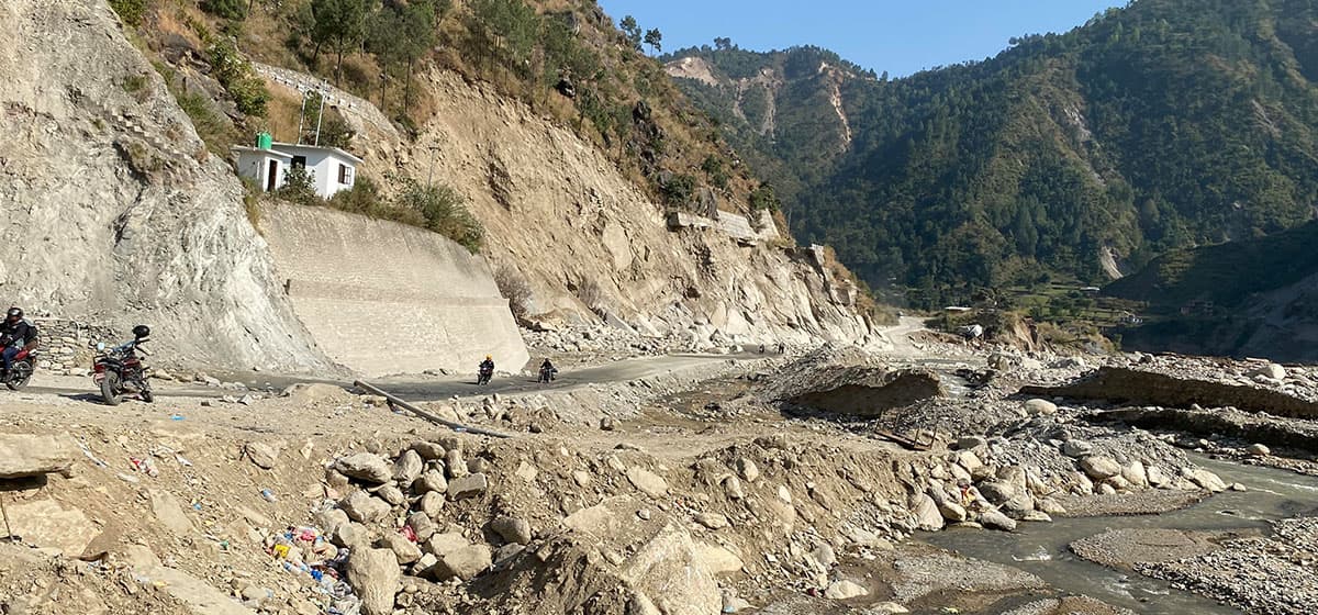 A road in a mountainous region covered with debris and rocks, with motorcycles passing through.