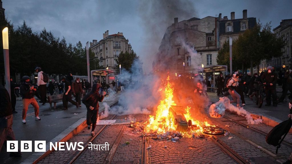 A large fire burning in the middle of a city street with people running nearby.