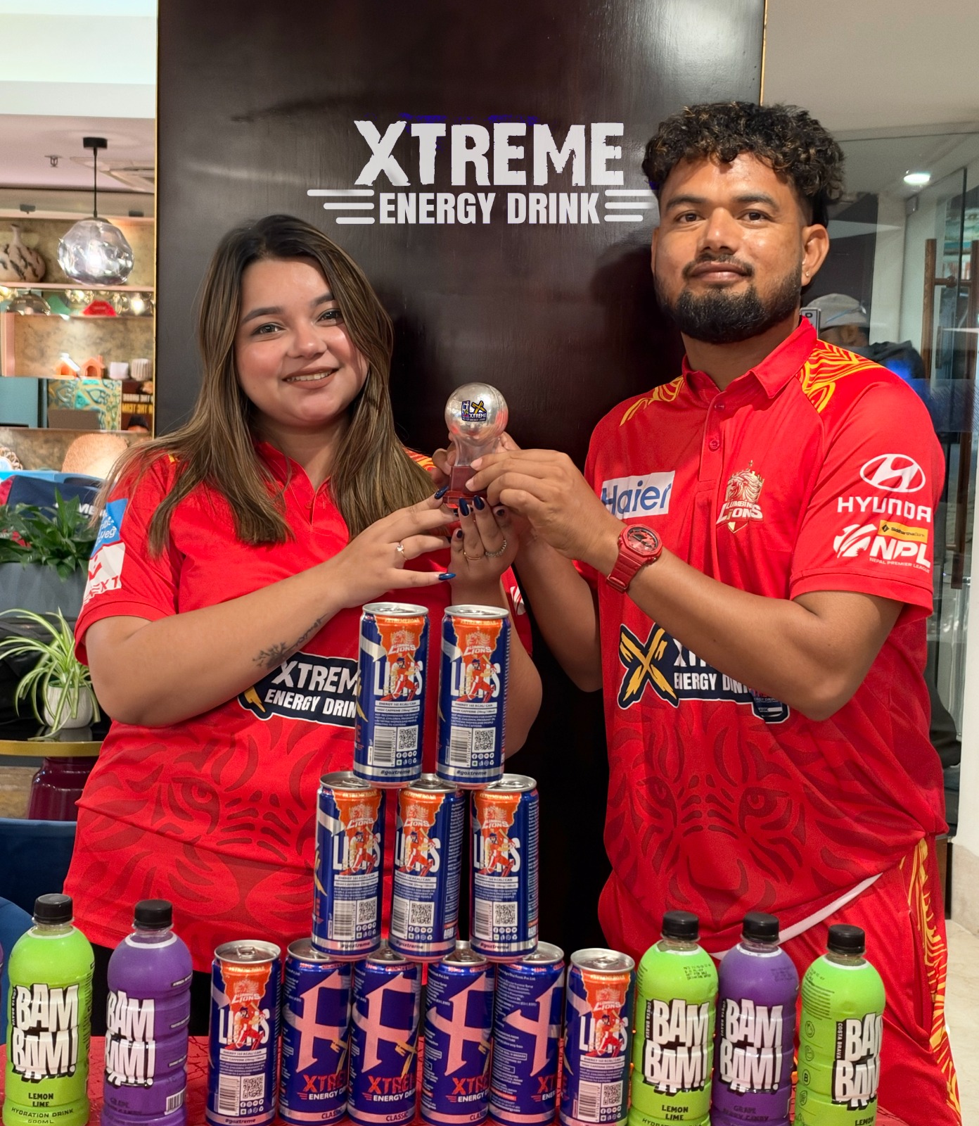 A man and a woman holding a Silver Ball trophy behind a display of Xtreme Energy Drink cans.
