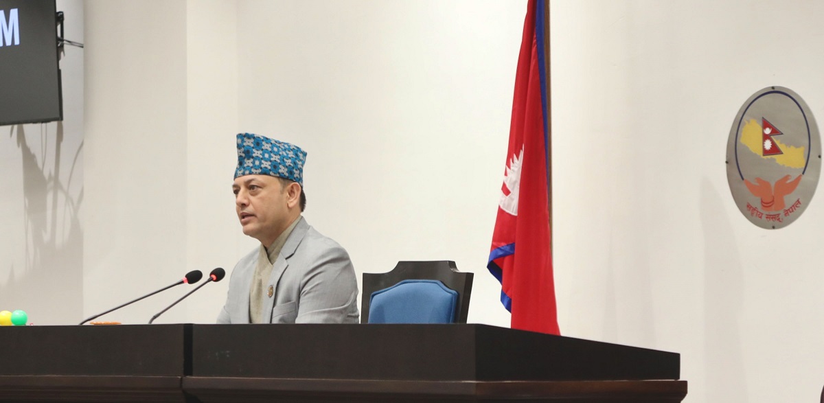 Dol Prasad Aryal seated behind microphones with the national flag of Nepal in the background.