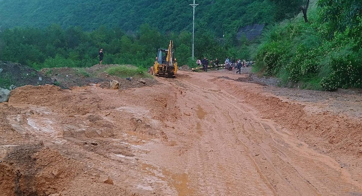 An excavator clearing a muddy road blocked by a landslide.