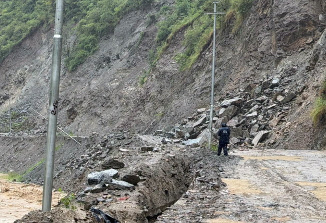A person standing near a landslide that has blocked the road.