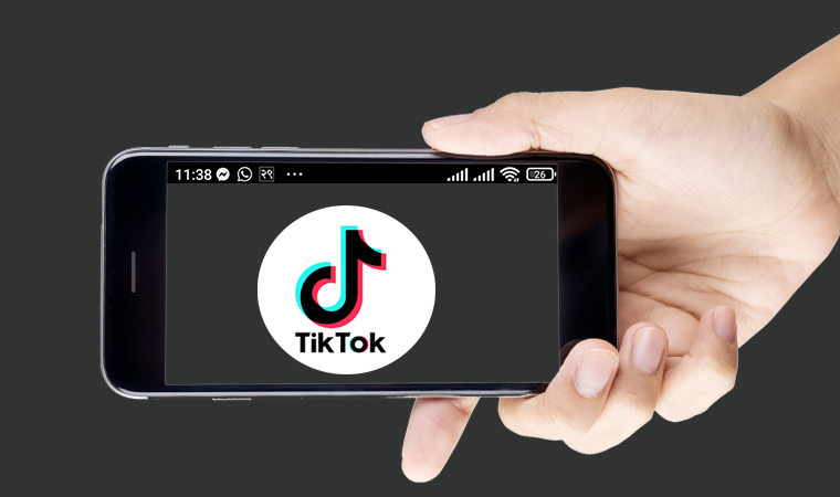 A hand holding a smartphone with the TikTok logo on the screen.
