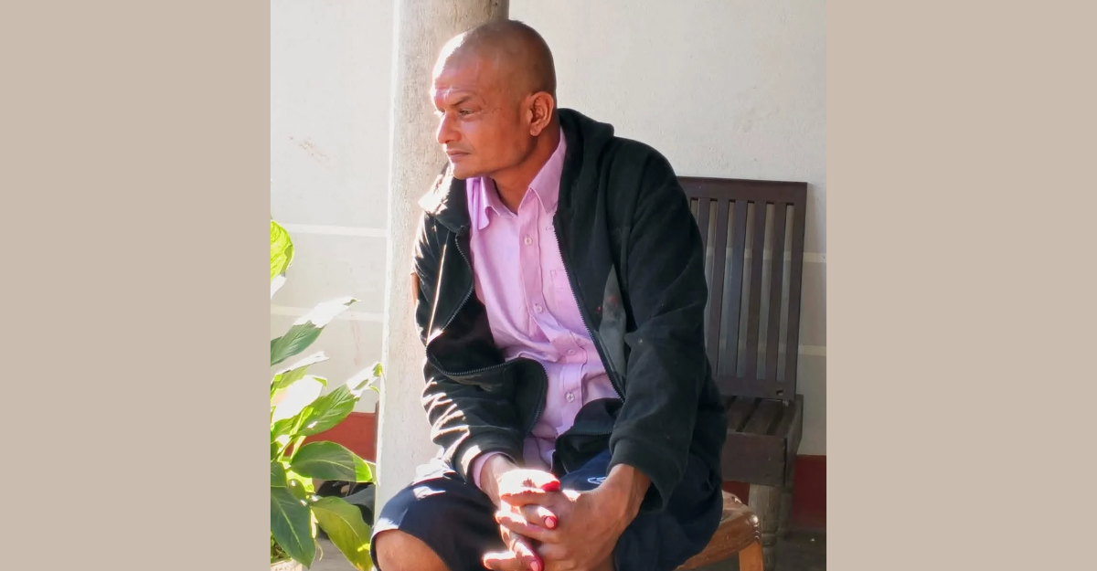 A man sits on a chair, looking away from the camera.