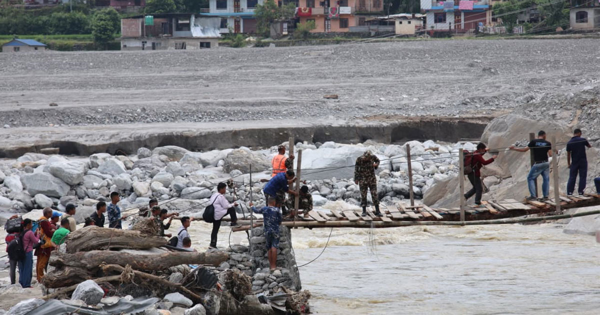 Pedestrians and security personnel crossing an interim wooden bridge over a rocky river.