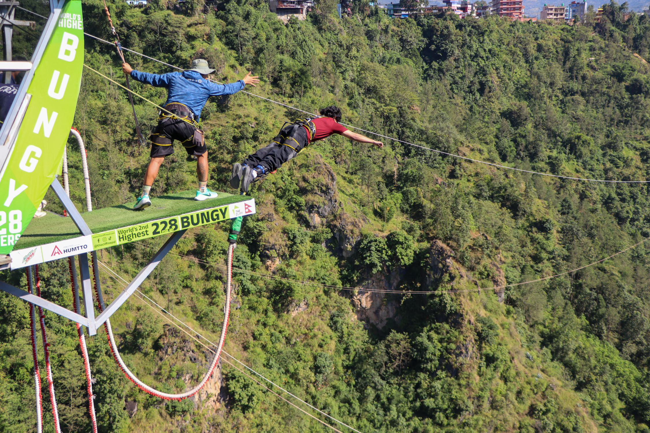 A person bungee jumping from a high platform over a forested valley.