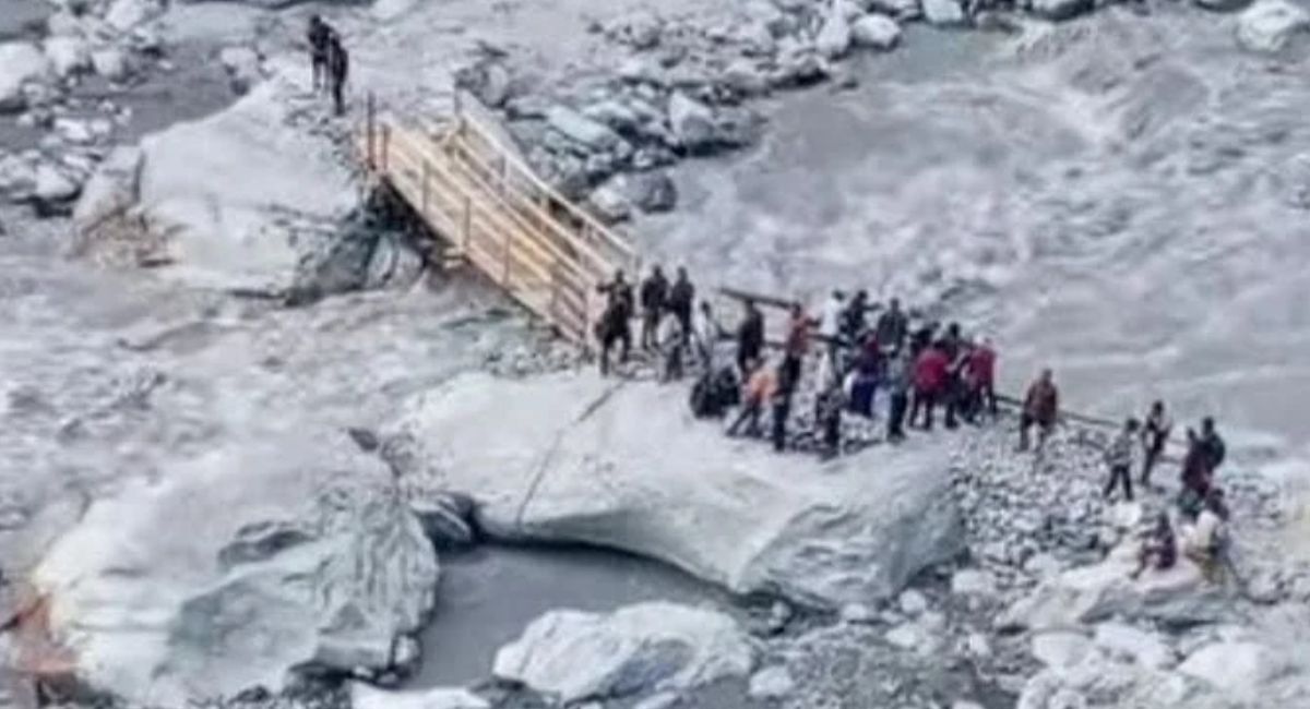 People crossing a temporary wooden bridge over a river.
