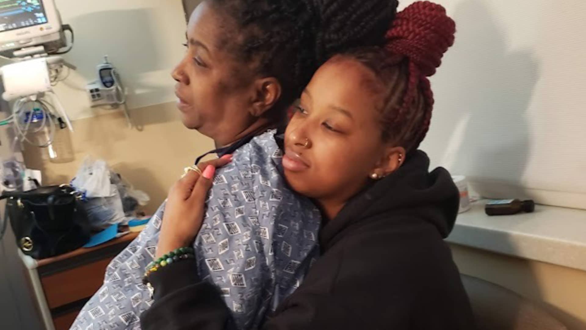 A person hugs an elderly relative in a hospital room.