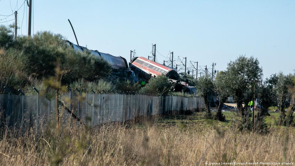 A derailed high-speed train lies on an embankment near a fence in Spain.