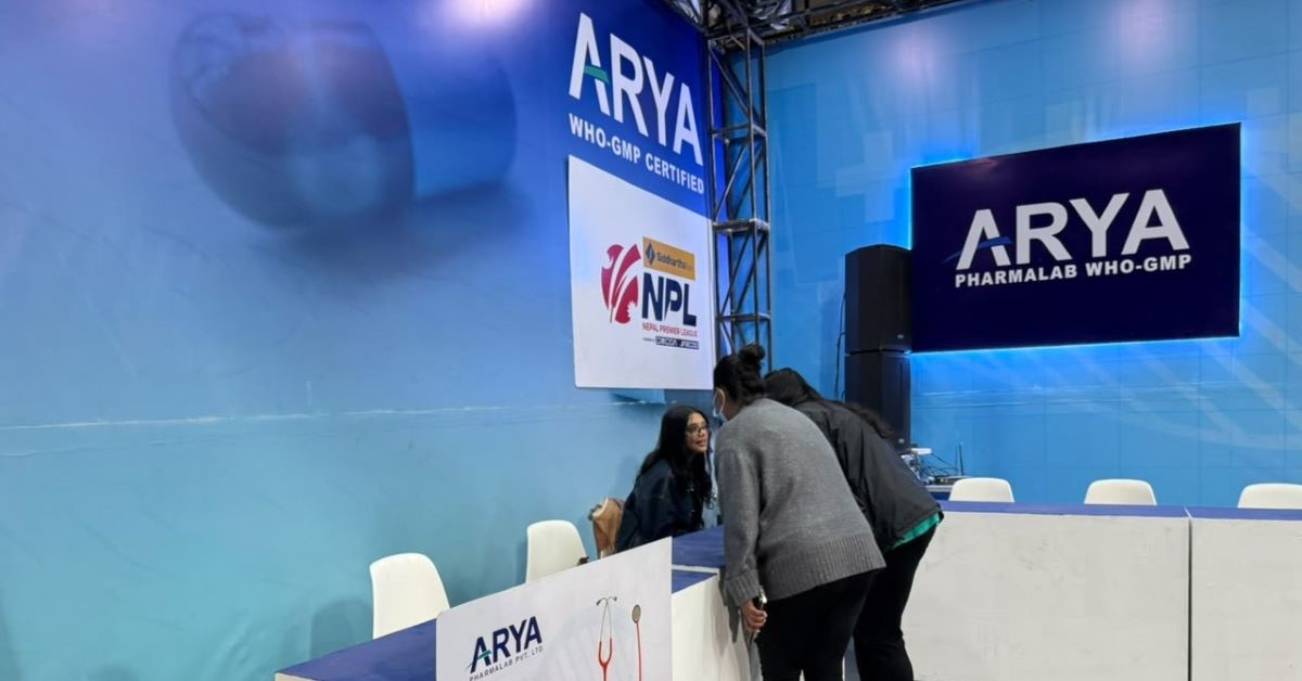 A close-up view of an Arya Pharmalab health consultation booth with branding and medical equipment visible.
