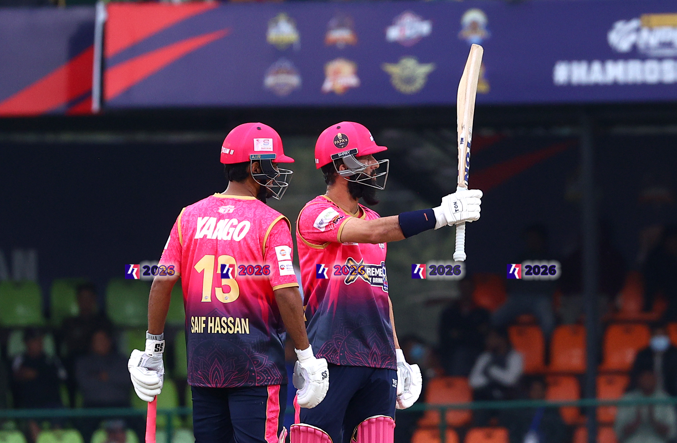 Two cricket players in pink jerseys, Saif Hassan and another teammate, standing on the field.